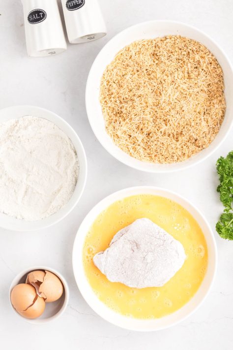 Pork chops being dipped from flour to egg to breadcrumb mixtures.