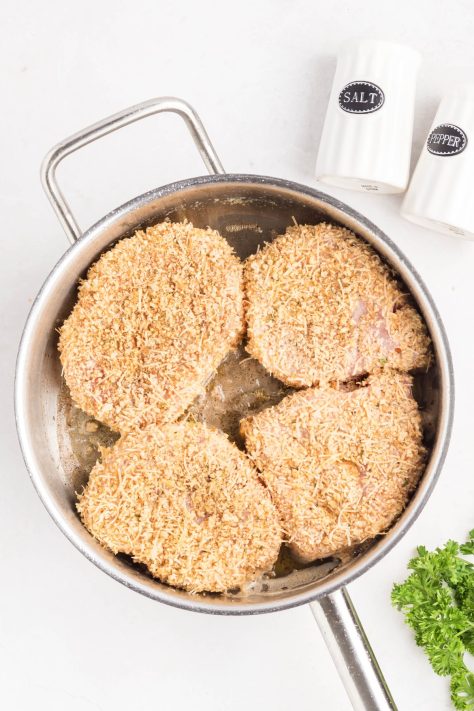 Breaded pork chops in a skillet.