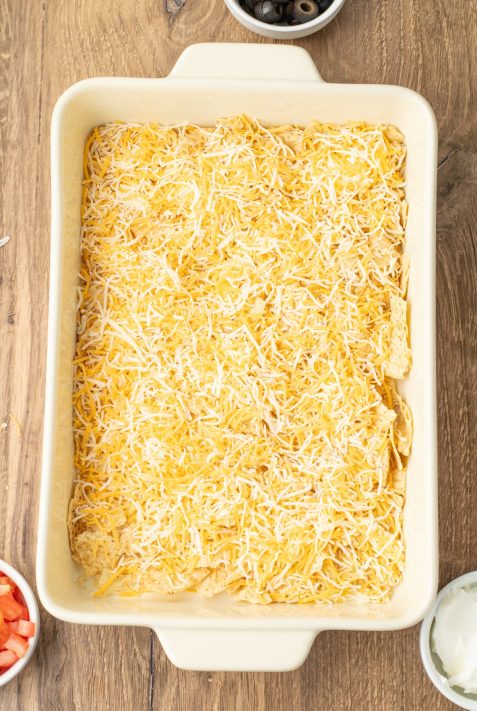 A baking dish with crushed chips and shredded cheese.
