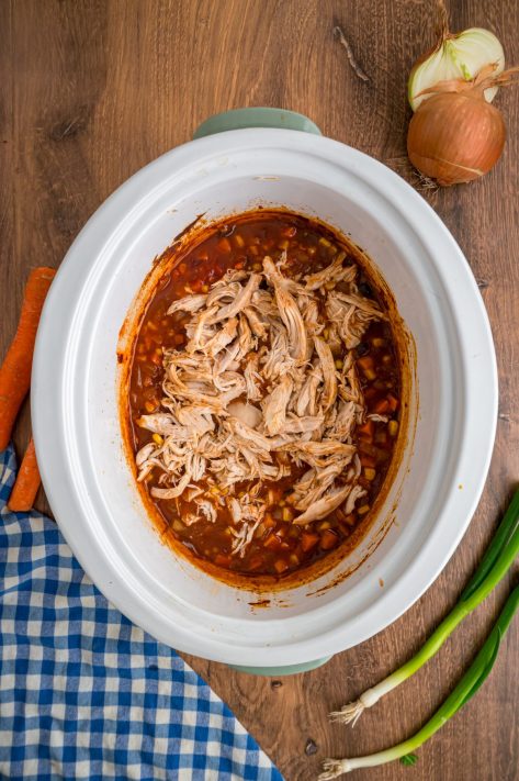 Shredded chicken being added back to a Slow Cooker.