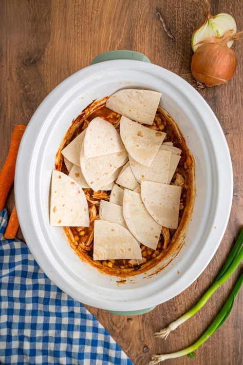 Cut up tortillas being added to a Slow Cooker mixture.