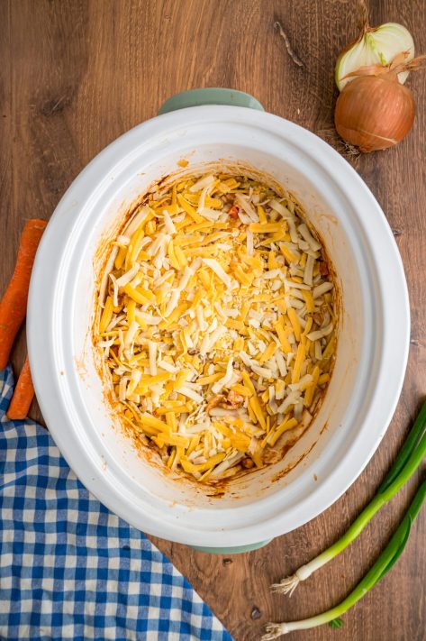 Shredded cheese on top of a casserole mixture in a Slow Cooker.