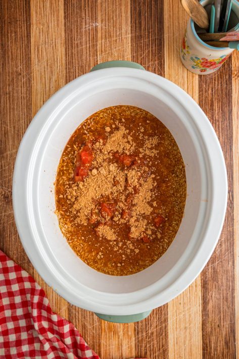 A slow cooker with chicken thigh pieces, Knorr Spanish Rice, chicken broth, salsa, water, and taco seasoning.