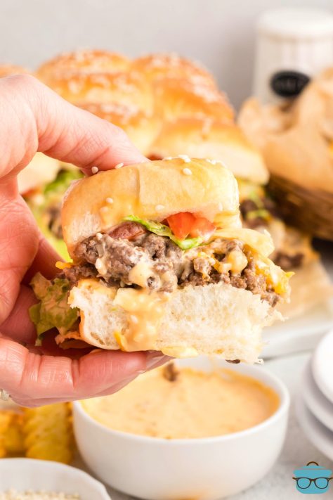 A hand dunking a Chopped Cheese Slider in a bowl of burger sauce for dipping.