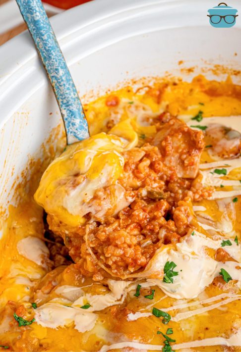 A serving spoon getting a scoop of Queso Chicken and Rice from the Slow Cooker.