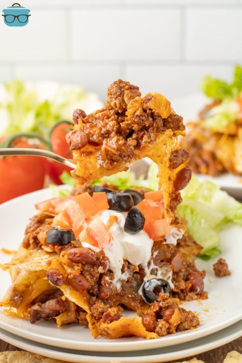 A fork holding a bite of Taco Casserole above the plates with a large serving of it.