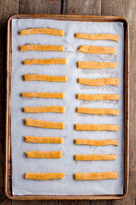 Cheese straws spaced on parchment paper.