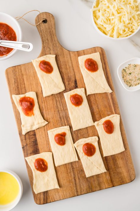 Pizza sauce being spread over crescent roll dough squares.
