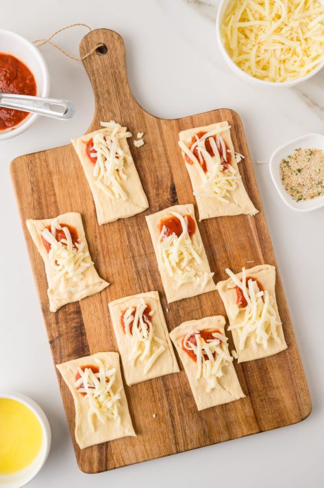 Shredded cheese on top of sauce on crescent roll dough.