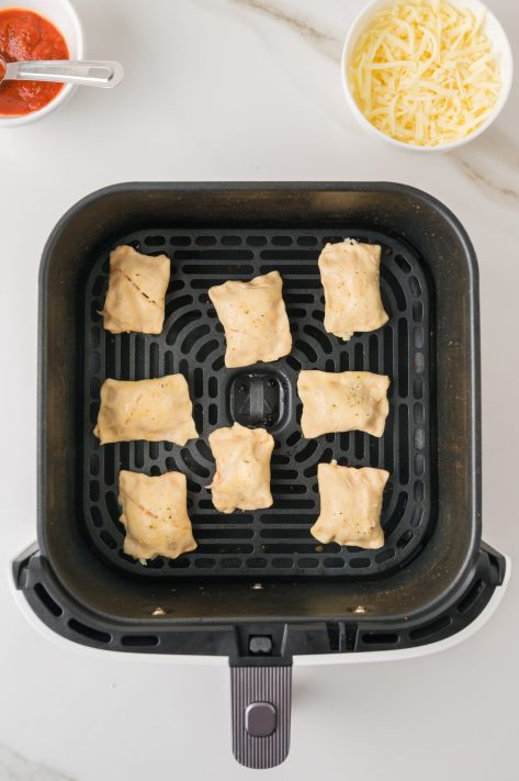 Unbaked Pizza Rolls in an Air Fryer basket.