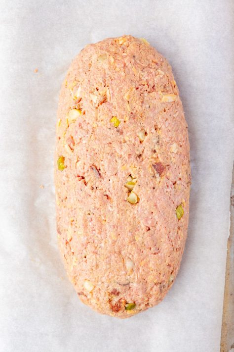 An unbaked loaf of meatloaf on a lined baking sheet.