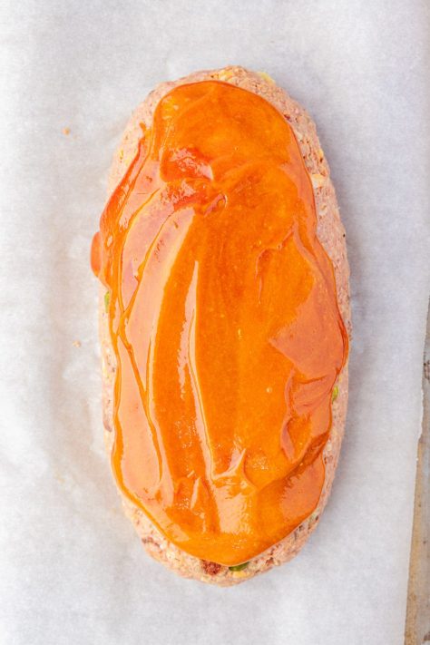 An unbaked loaf of meatloaf with a ketchup and mustard glaze on top.