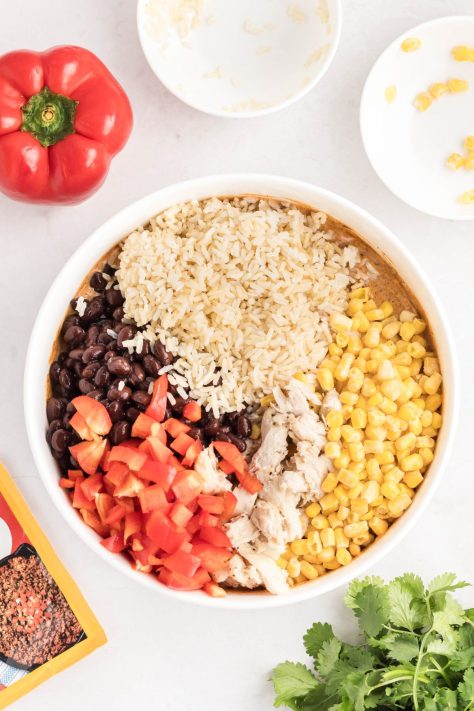 Chicken, beans, cooked rice, corn, and bell peppers being added to a bowl.