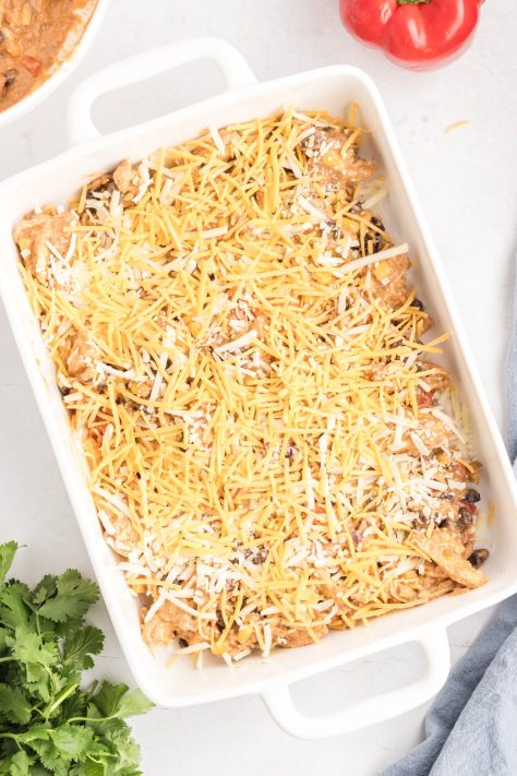 Shredded cheese over a chicken mixture and tortillas in a dish.