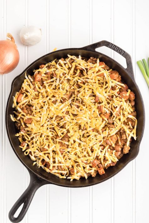 Shredded cheese on top of the casserole in a skillet.
