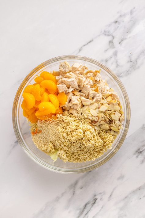 Ramen, coleslaw, chicken, oranges, and other ingredients in a bowl.