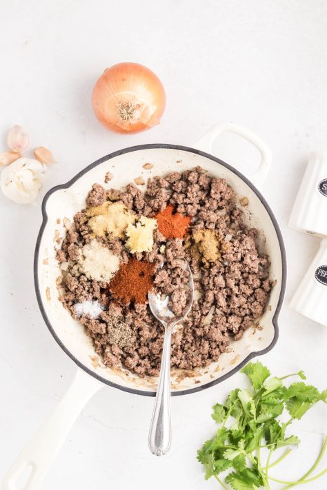 Garlic and seasonings being added to a ground beef and onion skillet.