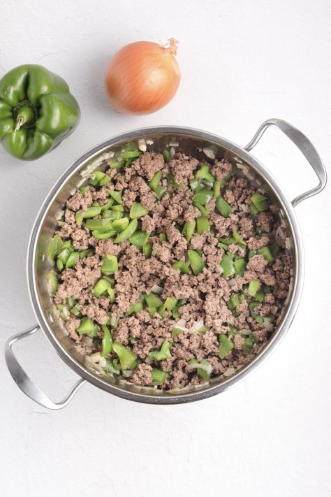A skillet with cooked green peppers, onions and ground beef.