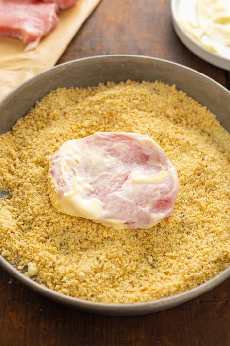 Mayo coated pork chop being coated in breadcrumb mixture.