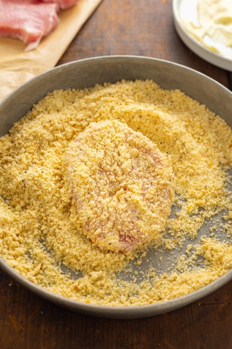 A pork chop being coated in a breadcrumb mixture.
