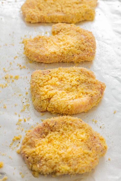 Coated pork chops on a lined baking sheet.