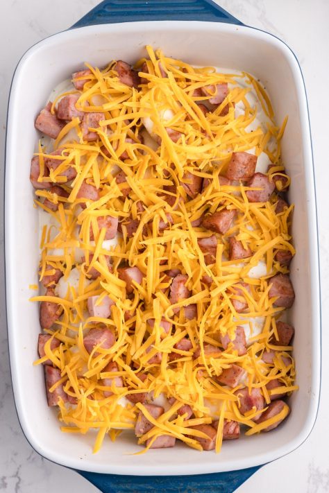 Layers of pierogis, kielbasa, cheese, and a sauce in a baking dish.