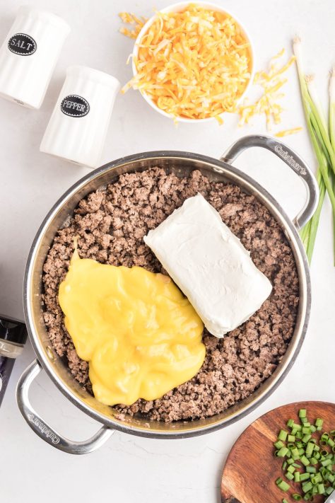 Cream of chicken soup and cream cheese being added to ground beef in a skillet.