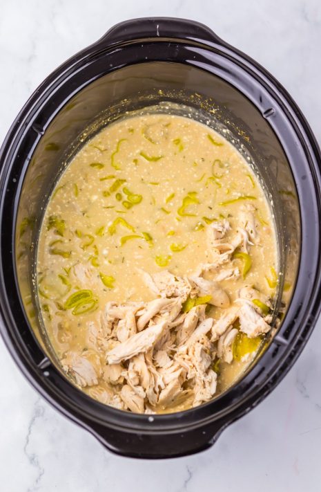 Shredded chicken being returned to a Crockpot full of chili.