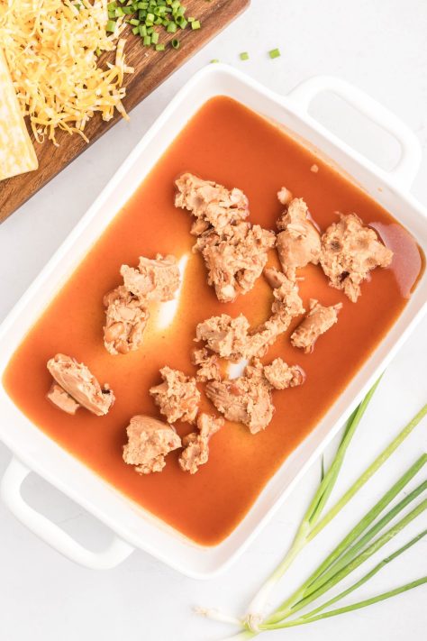 Refried beans and enchilada sauce in a baking dish.