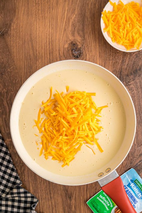 Shredded cheese being added to a sauce pan.