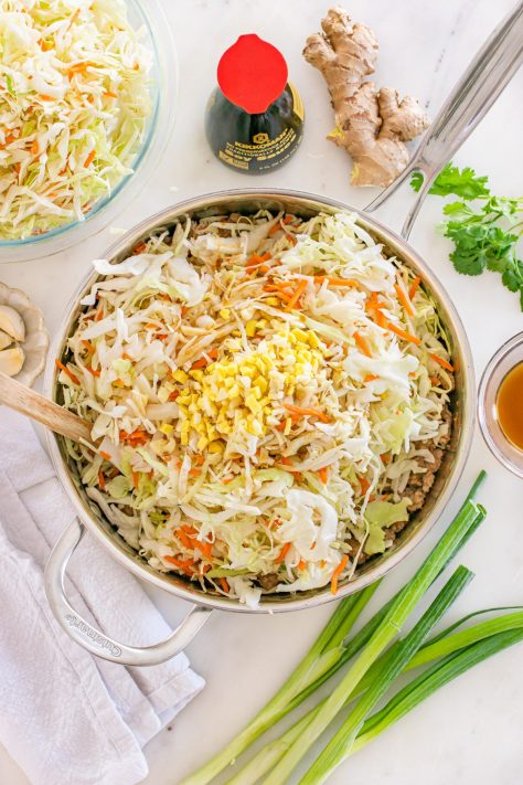 A skillet with ground pork, coleslaw, soy sauce, sesame oil, ginger, and garlic.