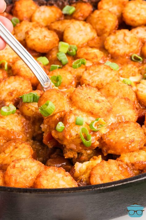 A spoon getting a scoop of Chili Cheese Dog Tater Tot Casserole from the skillet.