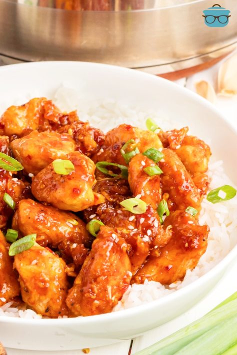 A bunch of Sweet Chili Chicken in a bowl with rice, green onions, and sesame seeds.