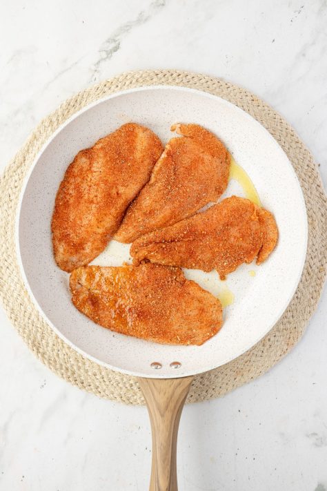 Seasoned chicken cooking in a skillet.