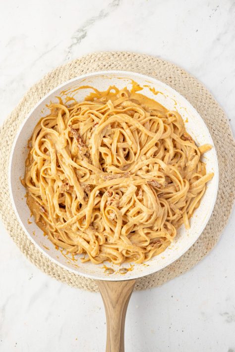 Cooked pasta being mixed into a sauce.