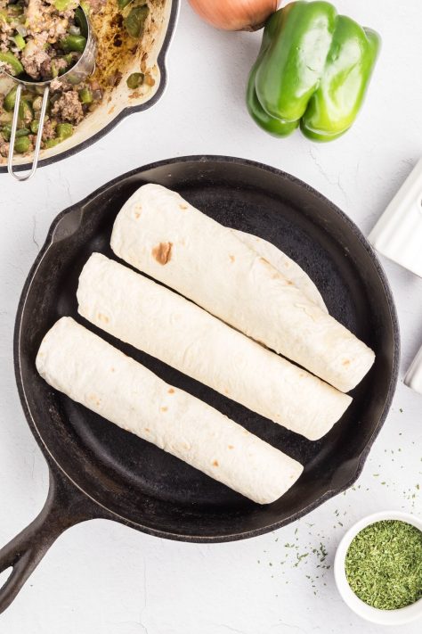 A skillet with tortillas stuffed with ground beef mixture.