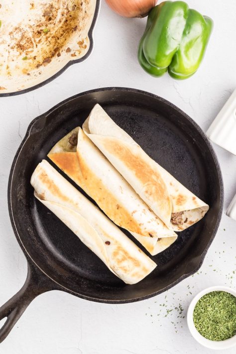 Rolled up Beef Enchiladas in a skillet.