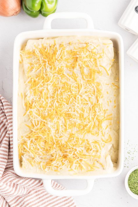 Shredded cheese sprinkled on top of a cheese sauce on enchiladas.
