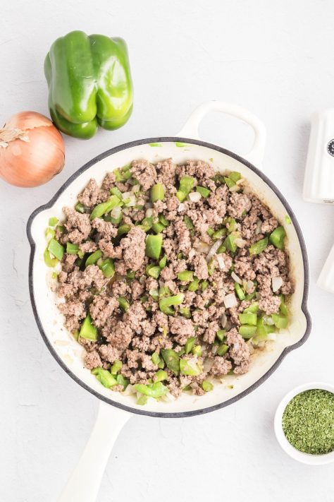 A skillet with cooked ground beef, onions, and green peppers.
