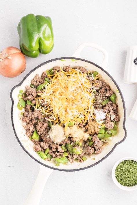 Shredded cheese is added to a skillet of ground beef, peppers, and onions.