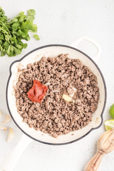 Tomato paste and garlic being added to the ground beef and onion mixture.