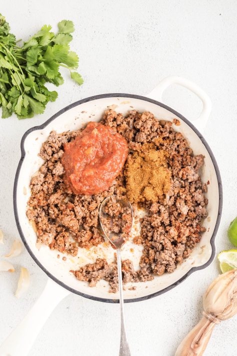 Water and taco seasoning added to a beef mixture in a skillet.