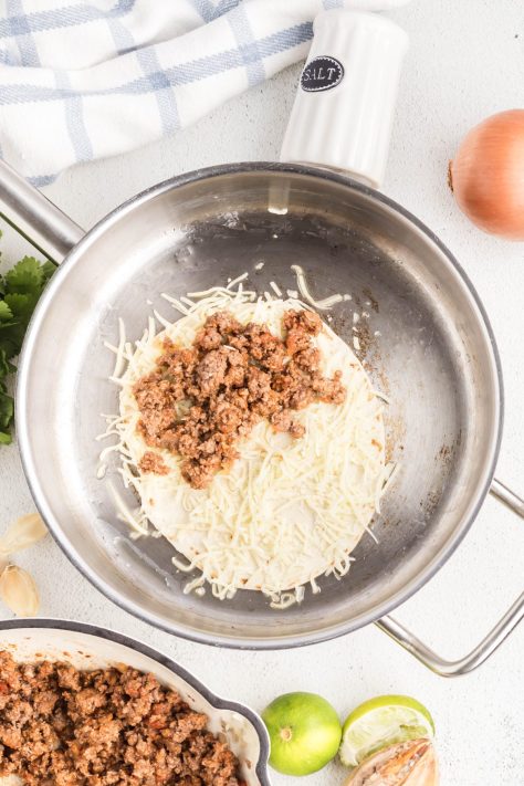 A tortilla with beef and cheese mixture in a skillet.
