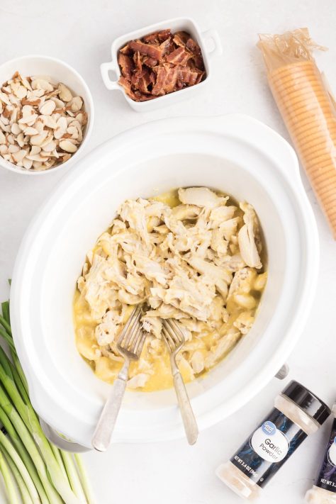 Two forks shredding chicken in a creamy mixture in a Slow Cooker.