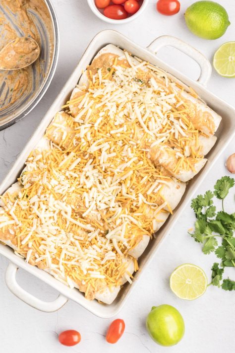 Shredded cheese added on top of enchiladas with sauce in a baking dish.
