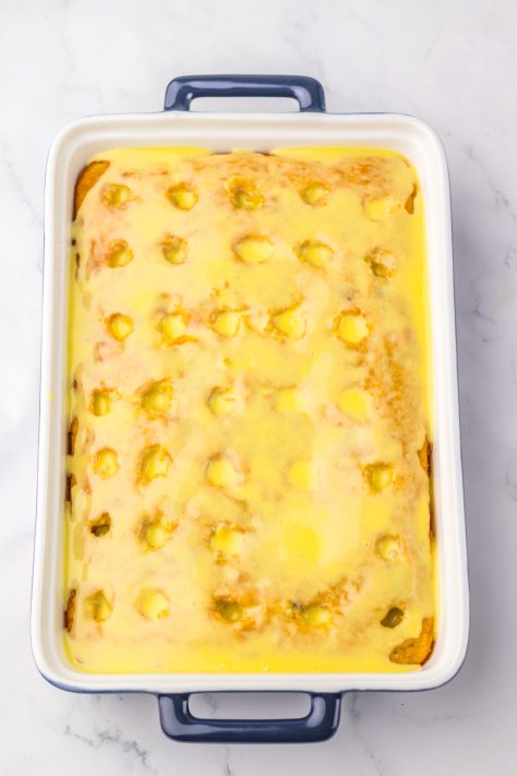 A bowl of sweetened condensed milk mixture being poured over the cake with holes.