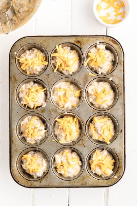 Sprinkled cheese on top of muffin batter in a muffin tin.