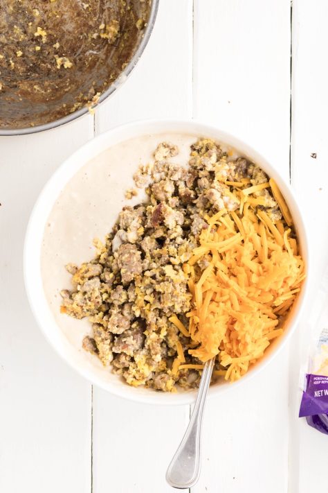Cheese, eggs, and sausage being added to a bowl of pancake batter.