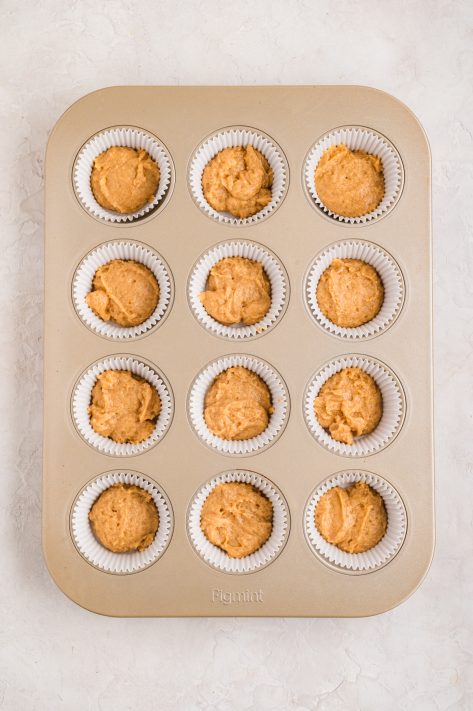 A muffin tin with lined wells with peanut butter muffin batter.