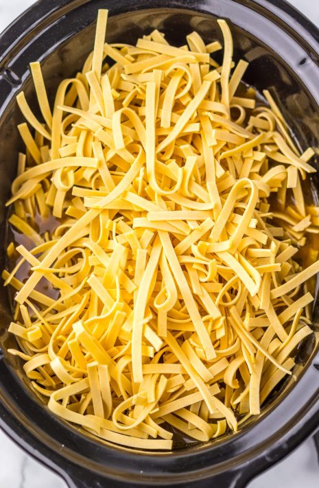 Uncooked egg noodles being added to a Slow Cooker.